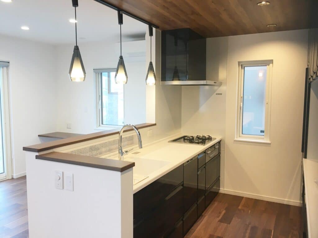 Modern kitchen with white island, dark glossy cabinets, and three geometric pendant lights above the counter.