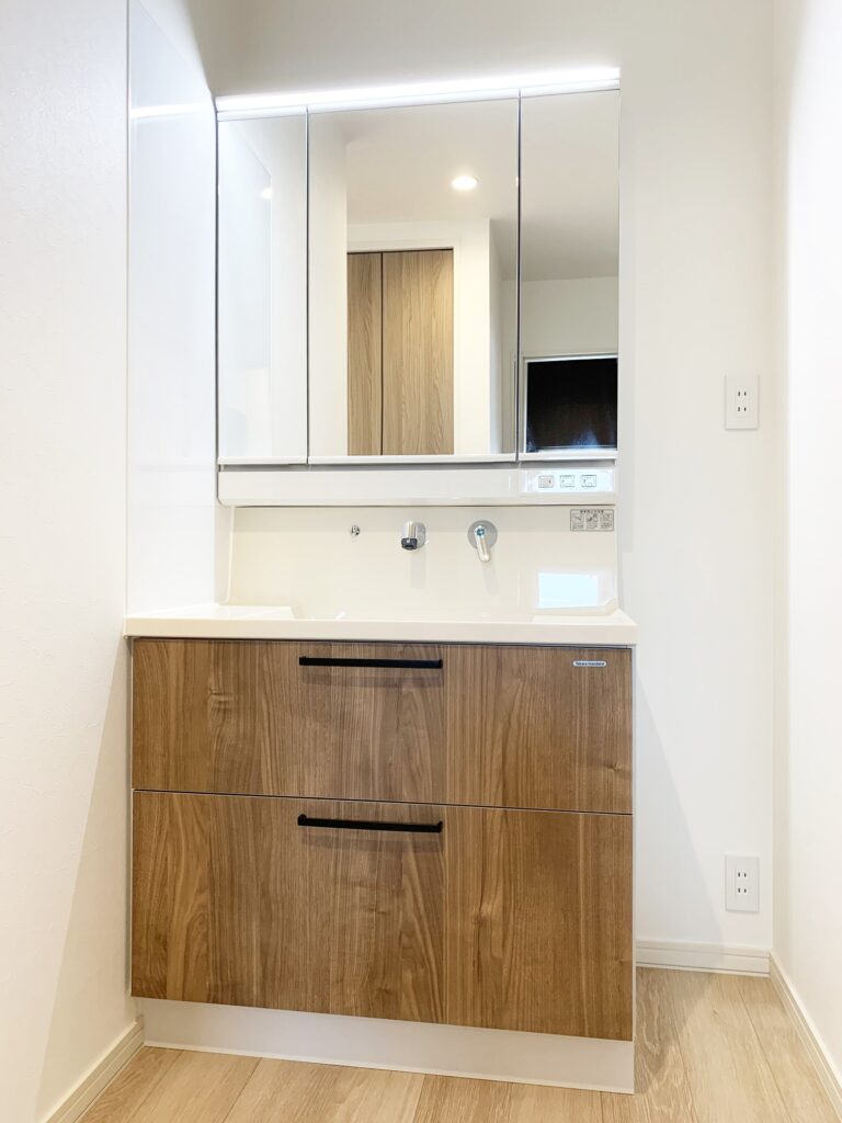 White bathroom vanity with mirrored medicine cabinet and wooden drawers, in a bright, modern space.