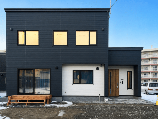 黒い外壁と木目の玄関ドアがある二階建て住宅の外観